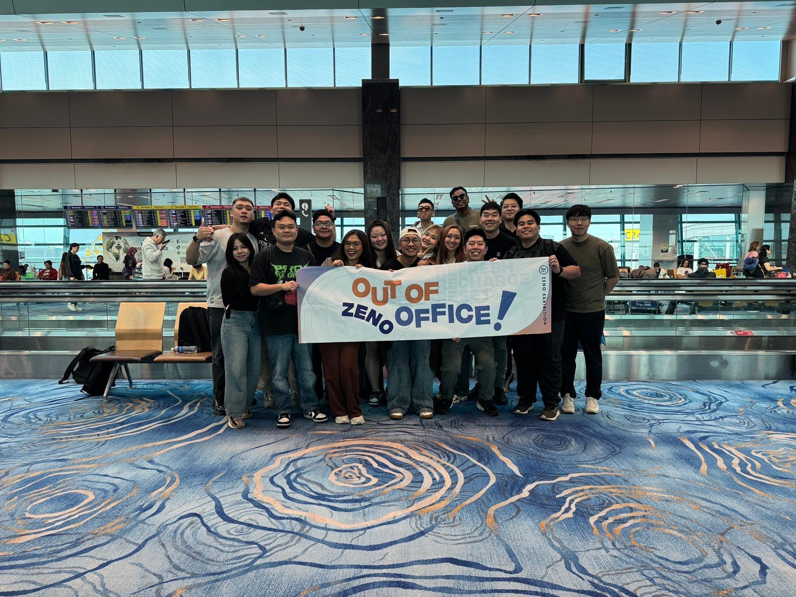 Zeno team at the airport with an Out of Zeno Office banner